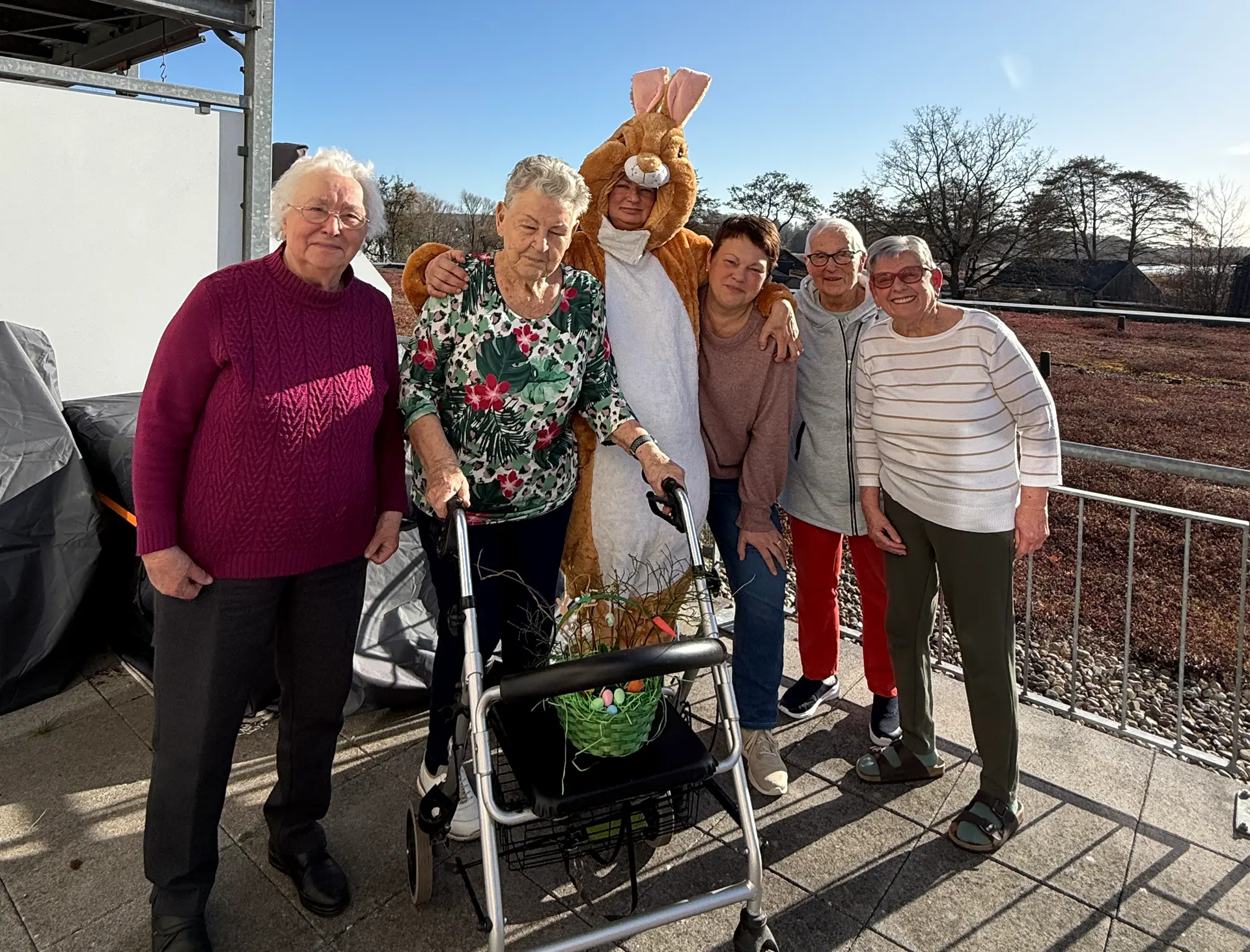 Eine kleine Gruppe strahlender Bewohner des betreuten Wohnens der Volkssolidarität in Binz hält stolz bunte, selbstgebastelte Osterkörbchen in den Händen. Im Vordergrund sitzt ein Vereinsmitglied im lebensgroßen, flauschigen Osterhasen-Kostüm.